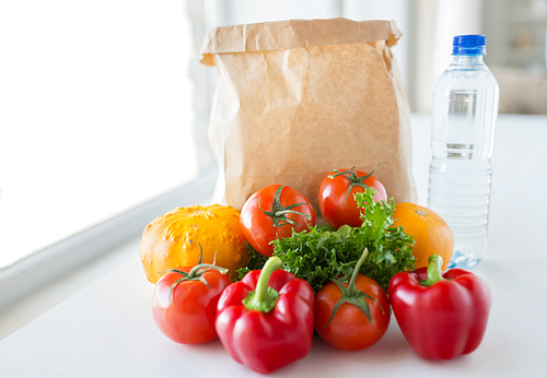 cooking, , vegetarian food and healthy eating concept - close up of paper bag with fresh ripe juicy vegetables and water bottle on kitchen table at home