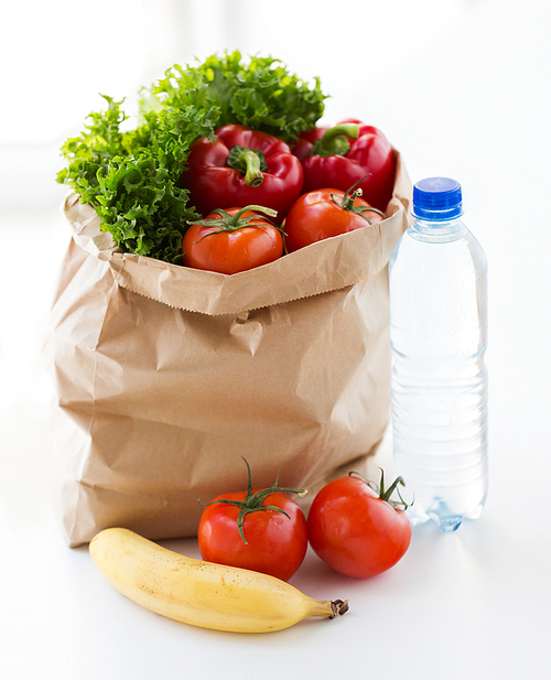 cooking, diet, vegetarian food and healthy eating concept - close up of paper bag with fresh ripe juicy fruits and vegetables and water bottle on kitchen table at home
