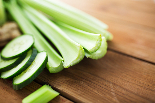 healthy eating, food, dieting and vegetarian concept - close up of green celery stems and sliced cucumber on wood