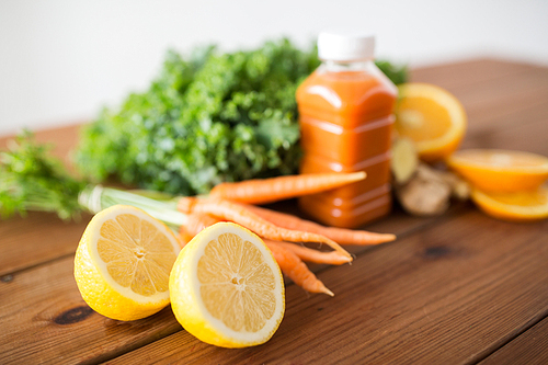 healthy eating, food, dieting and vegetarian concept - close up of lemon and bottle with carrot juice, fruits and vegetables on wooden table