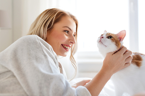 pets, morning, comfort, rest and people concept - happy young woman with cat in bed at home