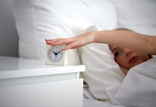 rest, sleeping, time and people concept - close up of young woman switching off alarm clock in bed at home bedroom