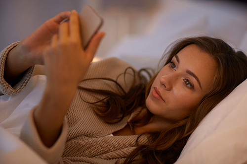 technology, internet, communication and people concept - happy smiling young woman texting on smartphone in bed at home bedroom at night
