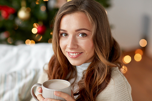 christmas, holidays and people concept - happy young woman with cup of coffee or cocoa drink at home