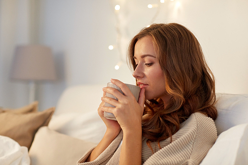 winter, leisure and people concept - happy young woman with cup of coffee or tea in bed at home bedroom