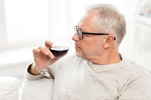 people, alcohol and drinks concept - senior man drinking red wine from glass at home