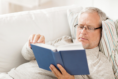age, leisure and people concept - senior man lying on sofa and reading book at home