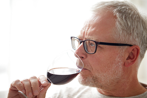 people, alcohol and drinks concept - close up of senior man drinking red wine from glass at home