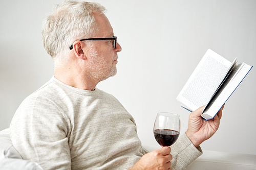 age, leisure and people concept - smiling senior man with wine glass reading book at home