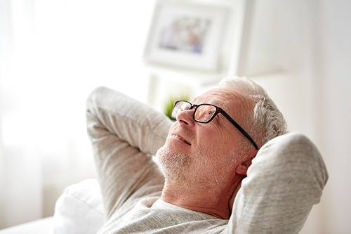 old age, comfort and people concept - smiling senior man in glasses relaxing on sofa at home