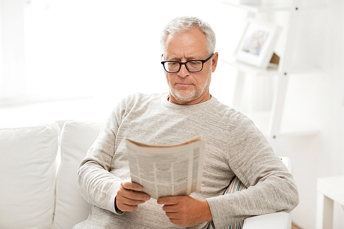 leisure, information, people and mass media concept - senior man in glasses reading newspaper at home