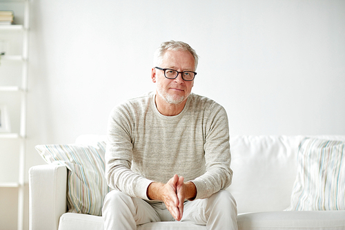 old age, comfort and people concept - smiling senior man in glasses sitting on sofa at home