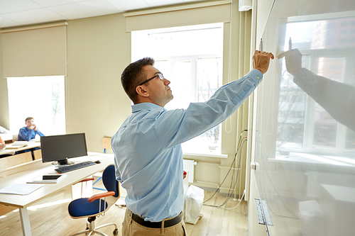 education, school, learning, teaching and people concept - teacher standing in front of students and writing something on white board in classroom