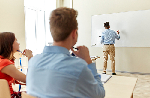 education, high school, learning, teaching and people concept - teacher standing in front of students and writing something on white board in classroom