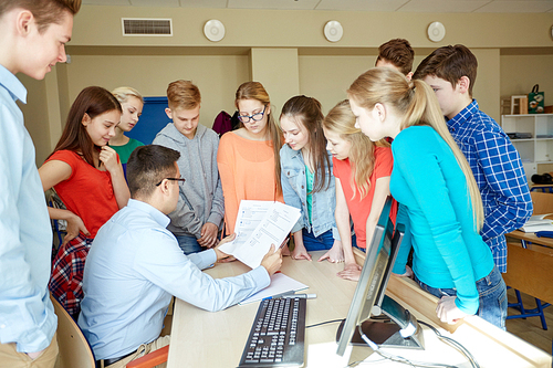 education, school, learning, teaching and people concept - group of students and teacher talking in classroom