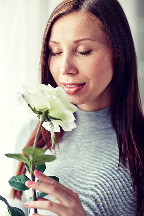 holidays, people and flowers concept - happy young woman smelling big white rose at home