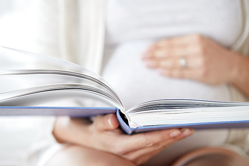 pregnancy, people and motherhood concept - close up of pregnant woman reading book