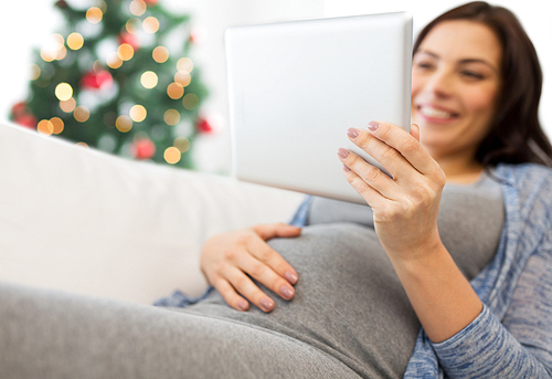 pregnancy, holidays, technology, people and expectation concept - close up of happy pregnant woman with tablet pc computer over christmas tree background
