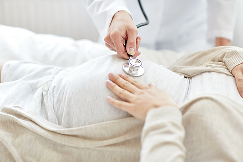 pregnancy, medicine, healthcare and people concept - close up of obstetrician doctor with stethoscope listening to pregnant woman baby heartbeat at hospital