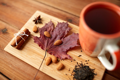 autumn and season concept - cup of tea, maple leaf and almond on wooden board