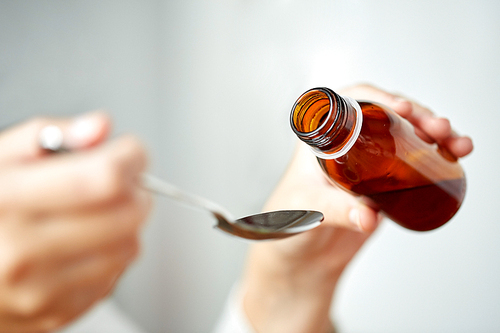 healthcare, people and medicine concept - woman pouring medication or antipyretic syrup from bottle to spoon