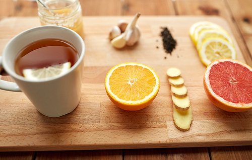 health, traditional medicine, folk remedy and ethnoscience concept - cup of ginger tea with honey, citrus and garlic on wooden background