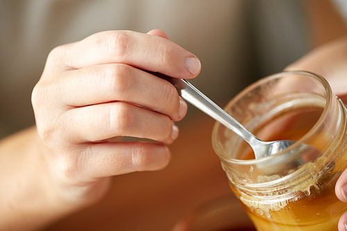 healthy food, eating and ethnoscience concept - close up of woman hands with honey and spoon