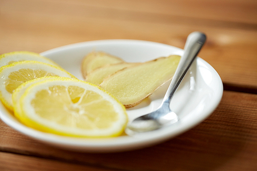 health, traditional medicine, folk remedy and ethnoscience concept - lemon slices and chopped ginger on plate with spoon