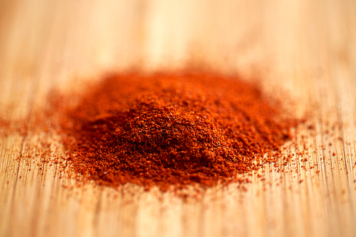 cooking, spice and ethnoscience concept - cayenne, chili pepper or paprika powder on wood