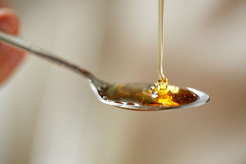 healthy food, eating and ethnoscience concept - close up of honey pouring to teaspoon