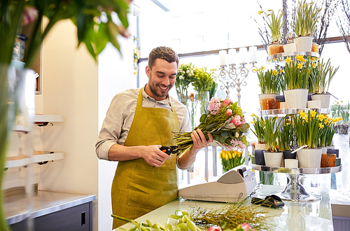 people, business, sale and floristry concept - happy smiling florist man making bunch and cropping stems by scissors at flower shop
