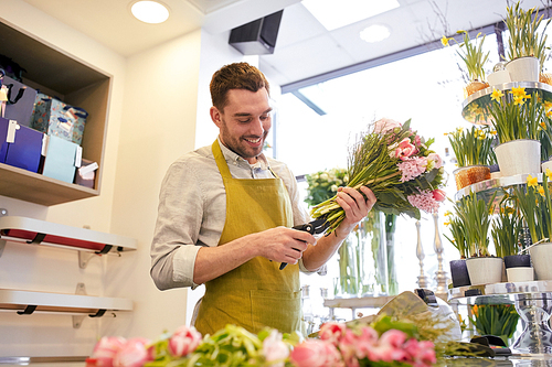 people, business,  and floristry concept - happy smiling florist man making bunch and cropping stems by scissors at flower shop
