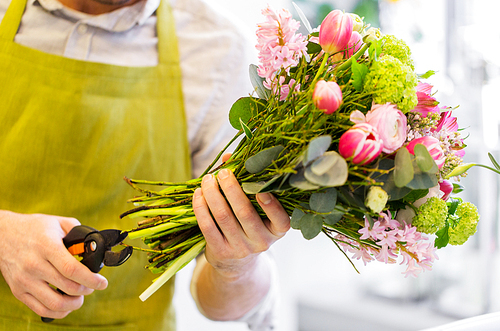 people, business,  and floristry concept - close up of florist man making bunch and cropping stems by pruner at flower shop