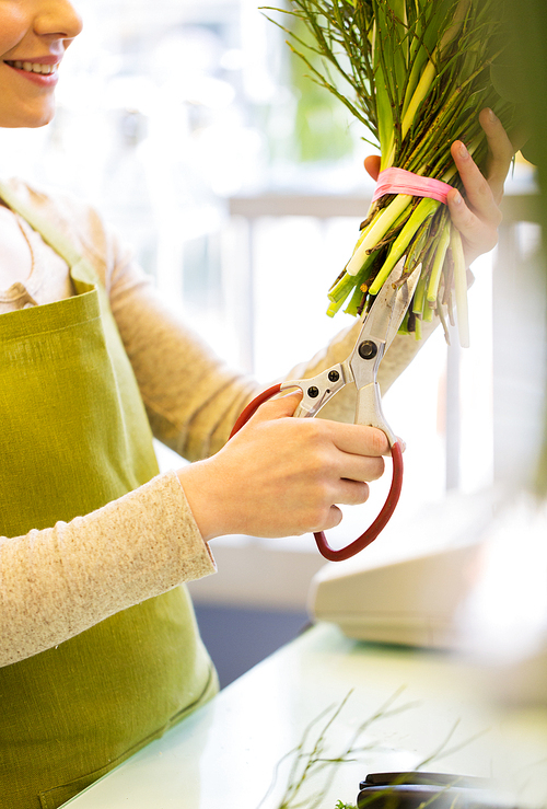 people, business,  and floristry concept - close up of florist woman making bunch and cropping stems by scissors at flower shop
