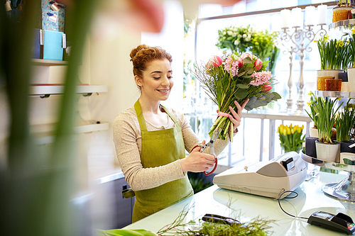 people, business,  and floristry concept - happy smiling florist woman making bunch and cropping stems by scissors at flower shop