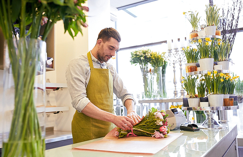 people, shopping, sale, floristry and consumerism concept - florist man wrapping flowers in paper at flower shop