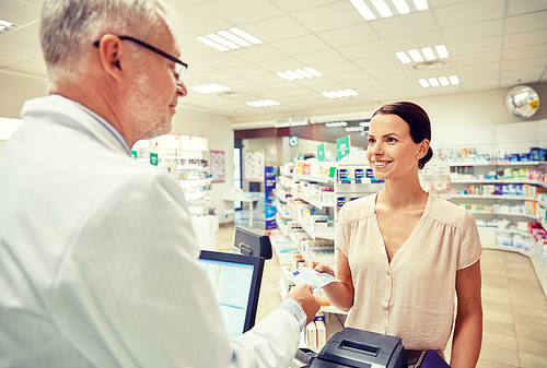 medicine, pharmaceutics, health care and people concept - smiling woman with wallet giving money to senior man pharmacist at drugstore cash register