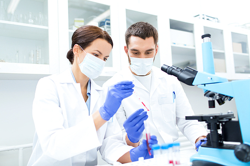 science, technology, biology and people concept - young scientists with pipette, test tube and microscope making research in clinical laboratory