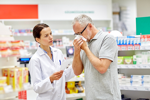 medicine, pharmaceutics, health care and people concept - pharmacist and sick senior man with flu blowing nose at pharmacy