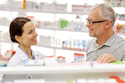 medicine, pharmaceutics, health care and people concept - happy pharmacist talking to senior man customer at drugstore