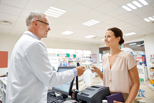 medicine, pharmaceutics, health care and people concept - smiling woman with wallet giving money to senior man pharmacist at drugstore cash register