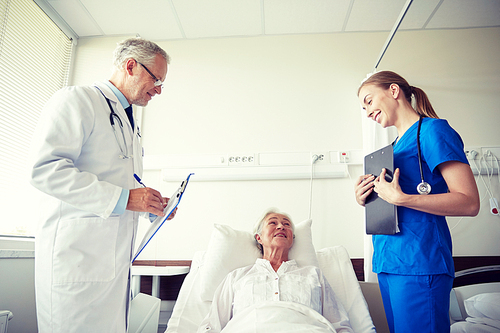 medicine, age, health care and people concept - doctor and nurse with clipboards visiting senior patient woman at hospital ward