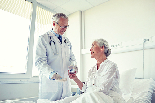 medicine, age, health care and people concept - doctor giving medication and water to senior woman at hospital ward