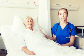medicine, age, support, health care and people concept - doctor or nurse visiting and cheering senior woman lying in bed at hospital ward