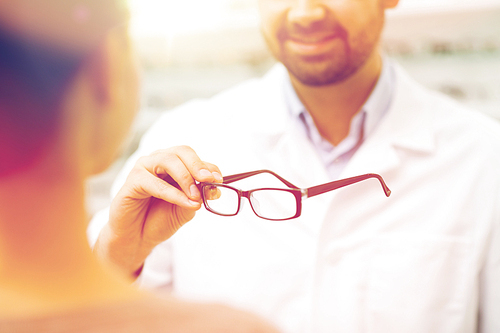health care, people, eyesight and vision concept - close up of optician showing glasses to woman at optics store