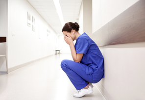 people, medicine, healthcare and sorrow concept - sad or crying female nurse at hospital corridor