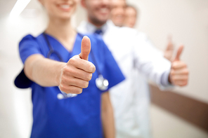 profession, people, healthcare, gesture and medicine concept - close up of happy medics or doctors at hospital corridor showing thumbs up