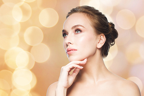 beauty, people and health concept - beautiful young woman touching her face over holidays lights background