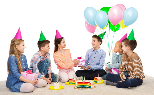 childhood, holidays, celebration, friendship and people concept - happy smiling children in party hats with cake giving presents at birthday party