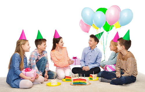 childhood, holidays, celebration, friendship and people concept - happy smiling children in party hats with cake giving presents at birthday party
